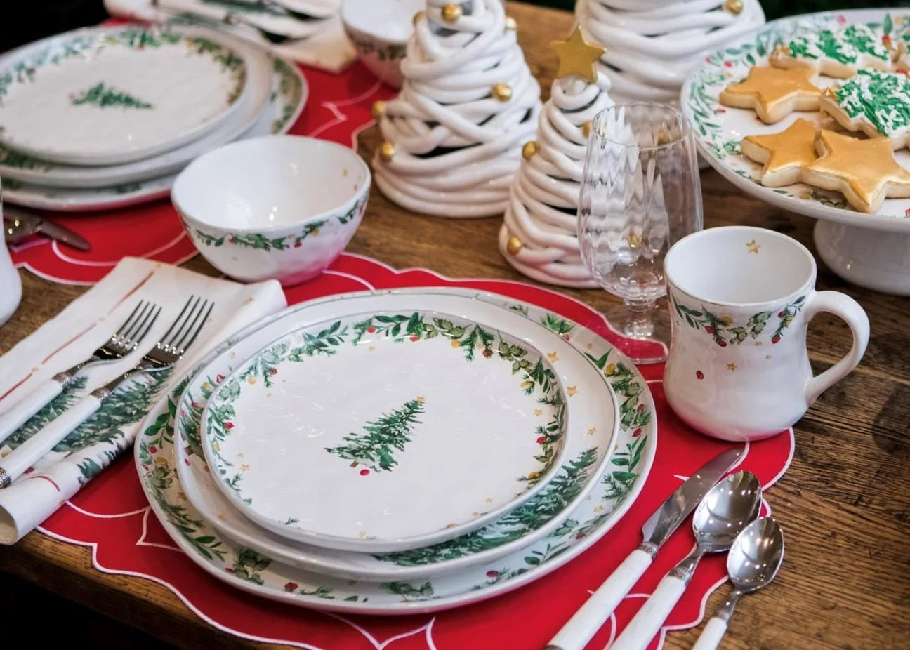 Christmas-themed table setting with ceramic trees and festive plates in front of a decorated tree.
